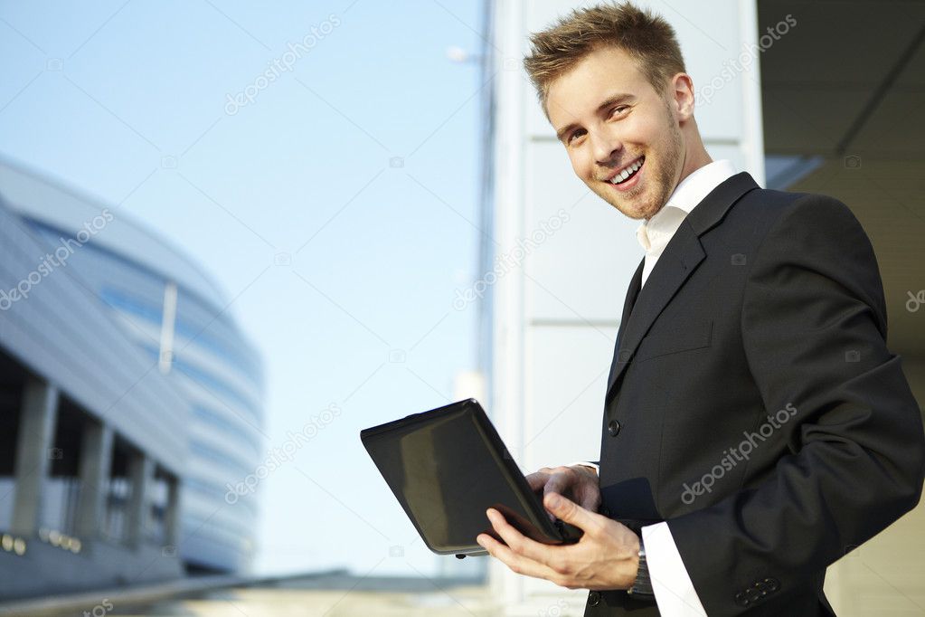 Closeup portrait of a happy young businessman using laptop on street