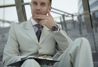 Handsome business man on the stairs reviewing his notes clipart