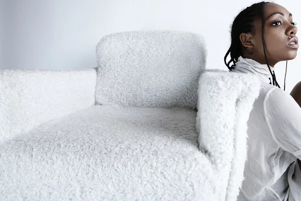 Afrikaanse vrouw zitten in de buurt van een witte fauteuil op een lichte achtergrond — Stockfoto