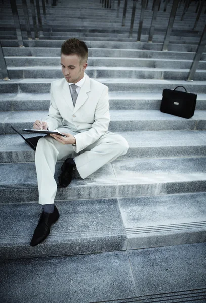 Hombre guapo ejecutivo de negocios sentado en las escaleras fuera de un edificio con —  Fotos de Stock