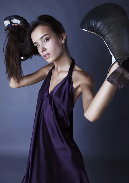 Sexy Brünette in Boxhandschuhen posiert im seidenen violetten Kleid. — Stockfoto