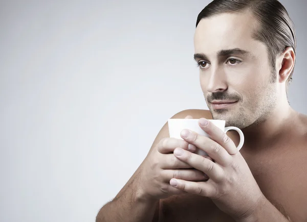 Szczęśliwy młody facet kaukaski na filiżankę kawy na białym tle na szary troska — Zdjęcie stockowe
