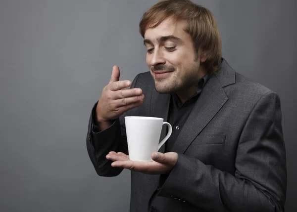 Szczęśliwy młody facet kaukaski na filiżankę kawy na białym tle na szary troska — Zdjęcie stockowe
