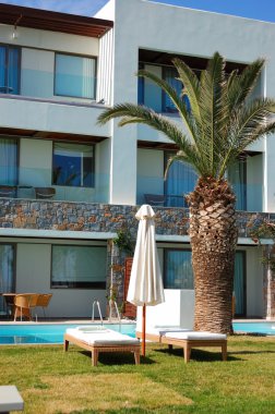 Sunbeds and palm tree at swimming pool of luxury hotel, Crete,