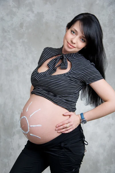 Een gelukkig zwangere meisje met de zon geschilderd op de buik — Stockfoto