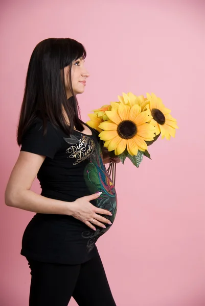 Beautiful pregnant woman holding belly with flowers — Stock Photo, Image