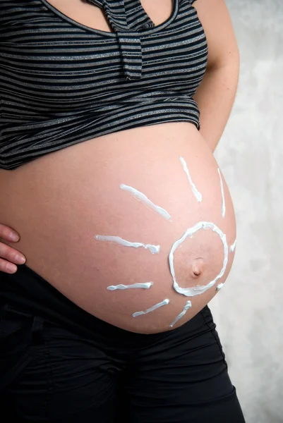 Uma menina grávida feliz com o sol pintado na barriga — Fotografia de Stock