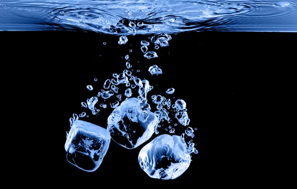Ледяные кубики падают в воду с брызгами — стоковое фото