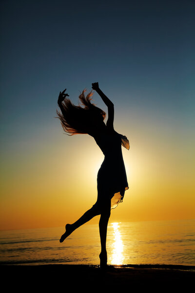 Girl dances on the beach at sunset. Natural light and dark. Artistic colors added. Vertical photo