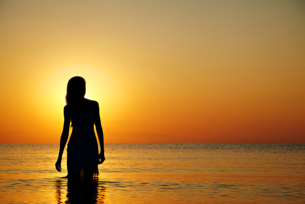 Silhouette of a girl in the water at sunset. Natural light and dark. Artistic colors added. Horizontal photo