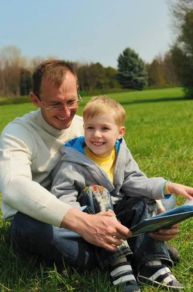 Little boy and his father are reading a book outdoor — Stock Photo, Image