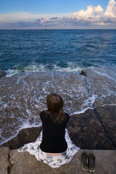 stock image Girl sits on the waterfront and looks at sea