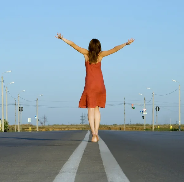 Девушка в красном платье ходит босиком по пустой дороге — стоковое фото