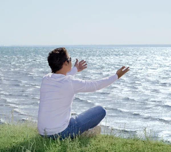 Молодой человек сидит на краю пропасти и смотрит на берег моря — стоковое фото
