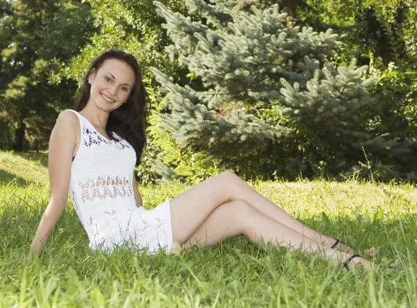 Roztomilá mladá žena sedí na travnaté hřiště v parku — Stockfoto