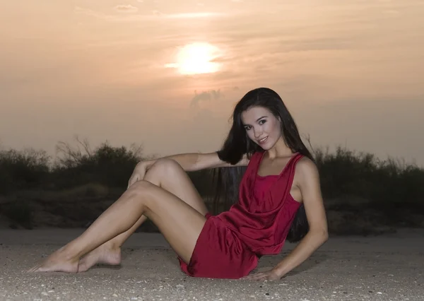 Милая женщина в красном платье позирует в пустыне на закате — стоковое фото