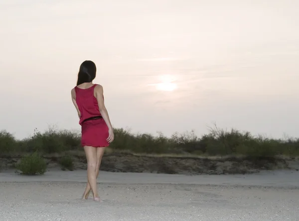 Schattig vrouwelijk in rode jurk lopen in de woestijn in zonsondergang — Stockfoto