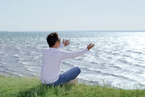 Jonge man zit op de afgrond en kijken op de kust — Stockfoto