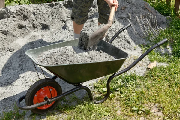 Ktoś napełniania taczki z szarego piasku — Zdjęcie stockowe