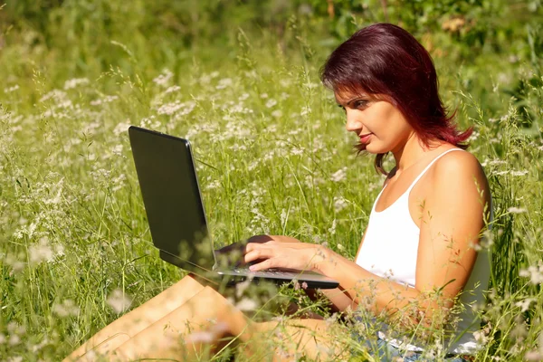 Mooie jonge vrouw zit op een gras in een park met de laptop. — Stockfoto