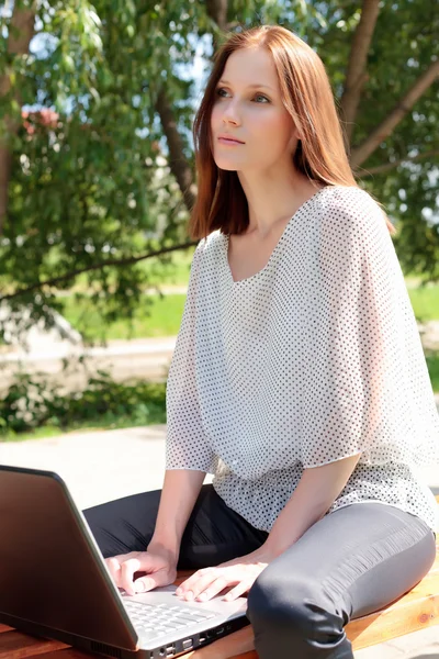 Mooie jonge vrouw met een laptop op park — Stockfoto