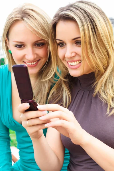Twee lachende meisjes kijken iets in mobiele telefoon — Stockfoto