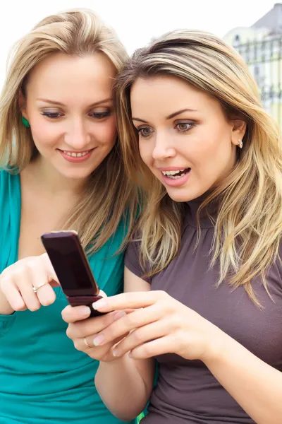 Две улыбающиеся девушки смотрят что-то в мобильном телефоне — стоковое фото