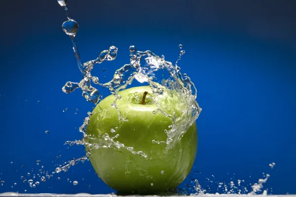 Pomme verte avec éclaboussure d'eau sur fond bleu — Photo