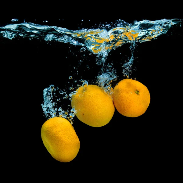 Frische Mandarinen fallen in Wasser mit Blasen auf schwarz — Stockfoto