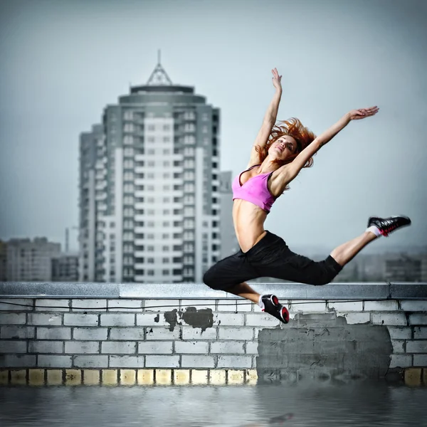 Girl jumping on the roof against city — Stock Photo, Image
