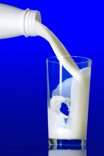 Latte versando in vetro su sfondo blu — Foto Stock