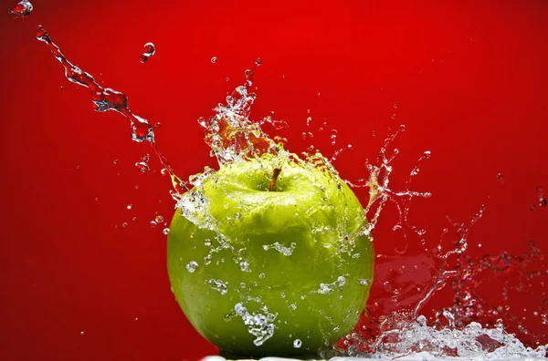 Maçã verde com respingo de água no fundo vermelho — Fotografia de Stock