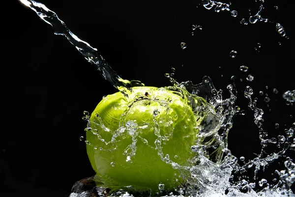 Зеленое яблоко с брызгами воды на черном фоне — стоковое фото