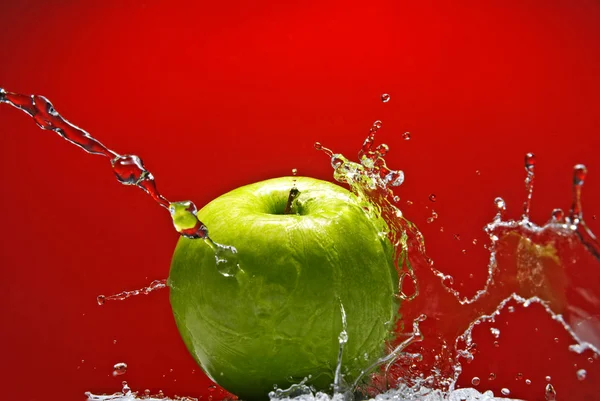 Зелене яблуко з водяним бризом на червоному тлі — стокове фото
