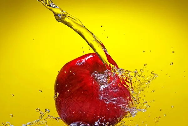 Красное яблоко с брызгами воды на желтом фоне — стоковое фото