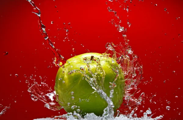 Green apple with water splash on red background — Stock Photo, Image
