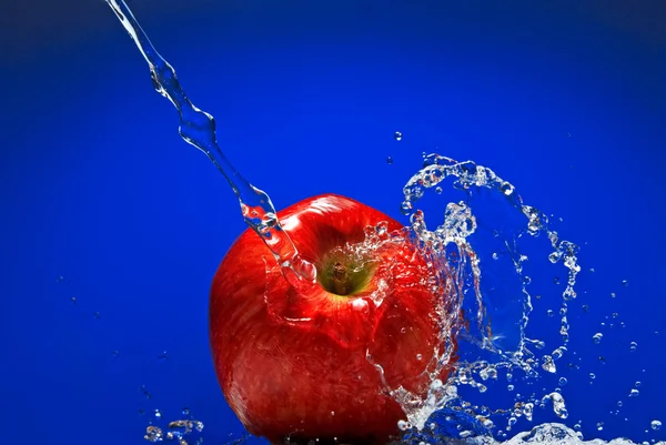 Rött äpple med vattenstänk på blå bakgrund — Stockfoto