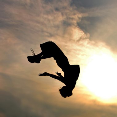 Silhouette of jumping man against sky and clouds clipart