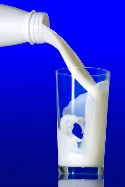Milk pouring from bottle into glass — Stock Photo, Image