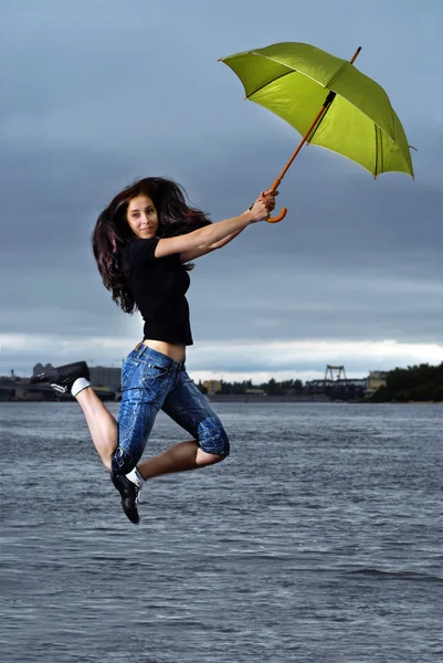 Fille sautant contre le ciel et l'eau avec parapluie — Photo