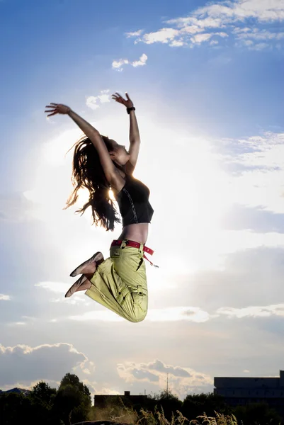 A young girl jumping in front of blue sky and sun — Stock Photo, Image
