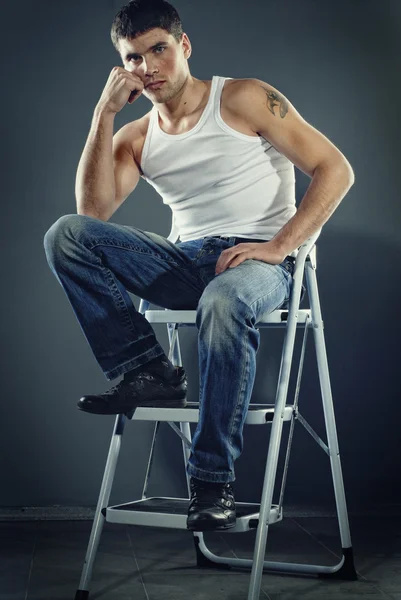 Attractive man in jeans sitting on stairs — Stock Photo, Image