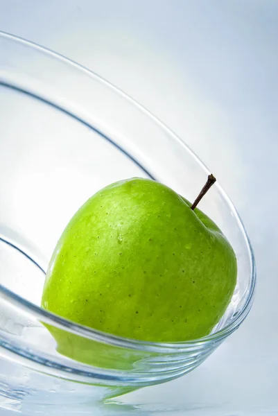 Зеленое яблоко в стеклянной пластине на голубом фоне — стоковое фото