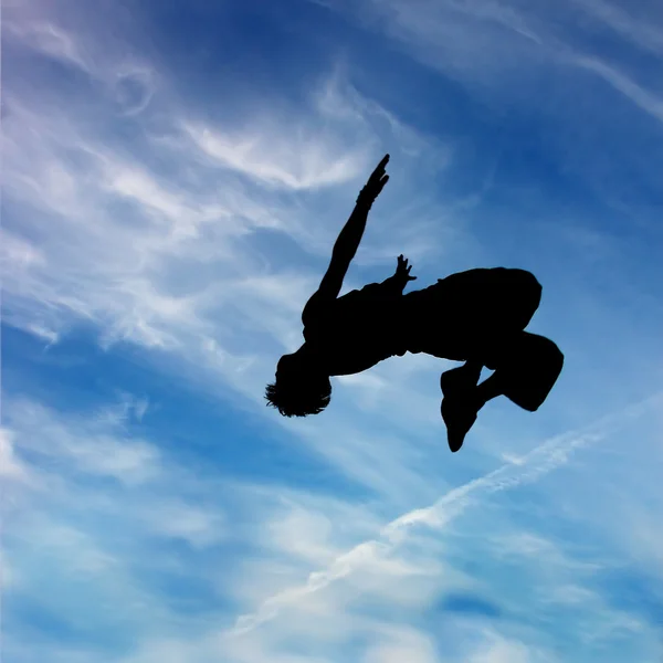 Sylwetka skoków człowiek przeciw błękitne niebo i chmury — Zdjęcie stockowe