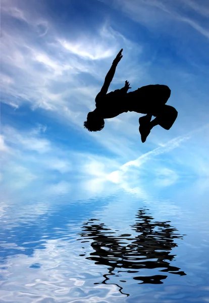 Silueta skákání muž proti modré obloze a mraky — Stock fotografie