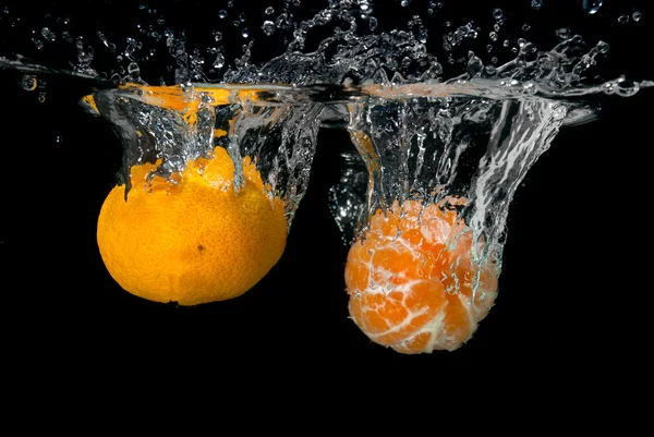 Fresh tangerines dropped into water with bubbles on black — Stock Photo, Image