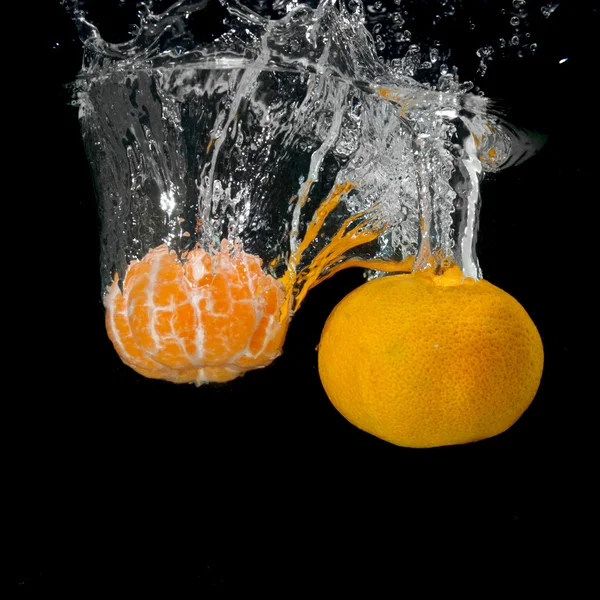 Färska mandariner tappade i vatten med bubblor på svart — Stockfoto