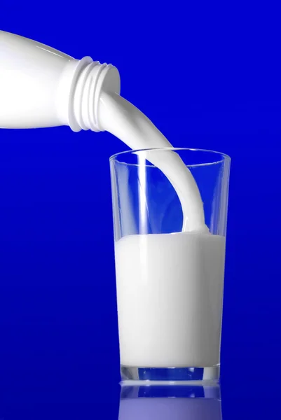 Milk pouring from bottle into glass on blue background — Stock Photo, Image