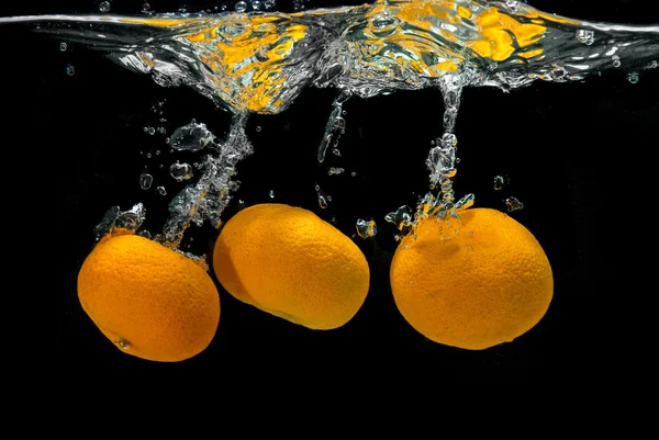 Mandarini freschi caduti in acqua con bolle sul nero — Foto Stock