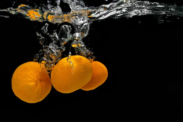 Las mandarinas frescas cayeron en el agua con burbujas en negro — Foto de Stock